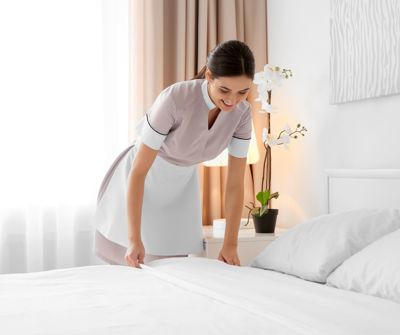 A maid at work in a hotel tidying the bed